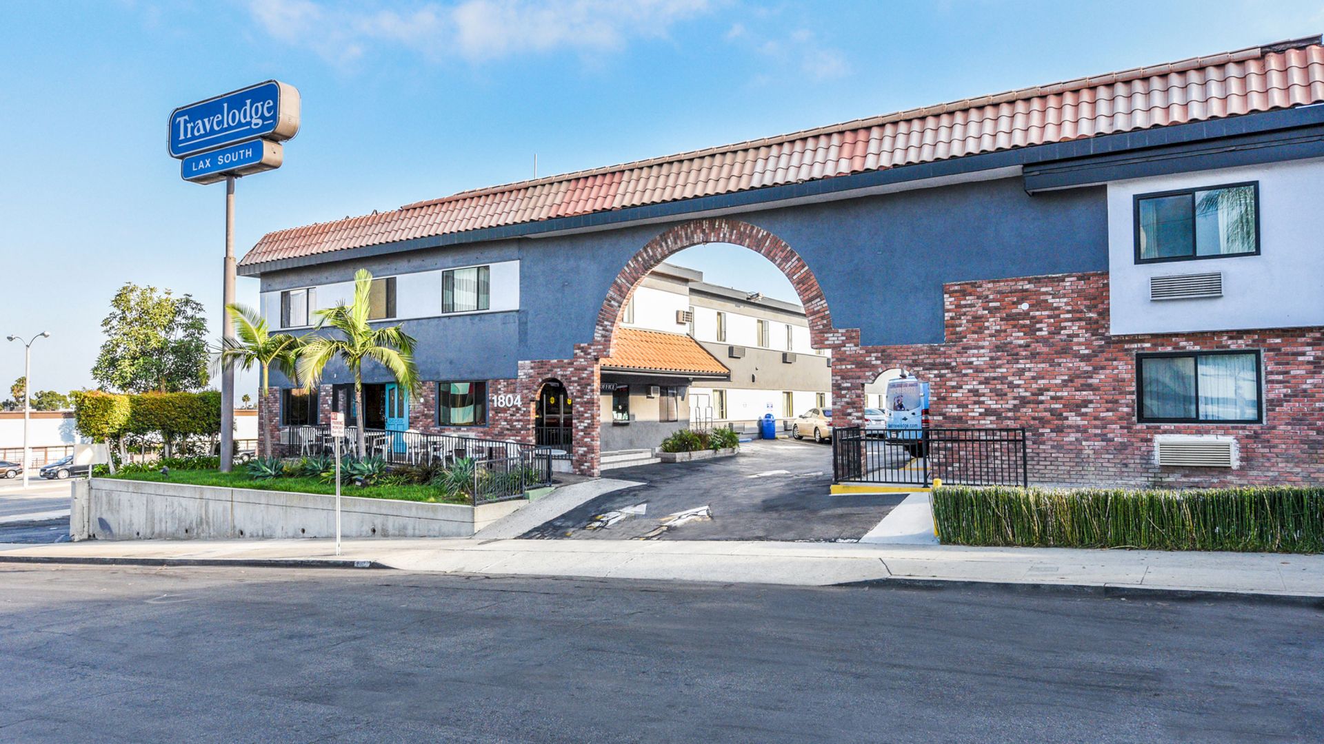 This image shows the exterior of a Travelodge hotel with a distinctive archway and a blue sign, set under a partly cloudy sky.