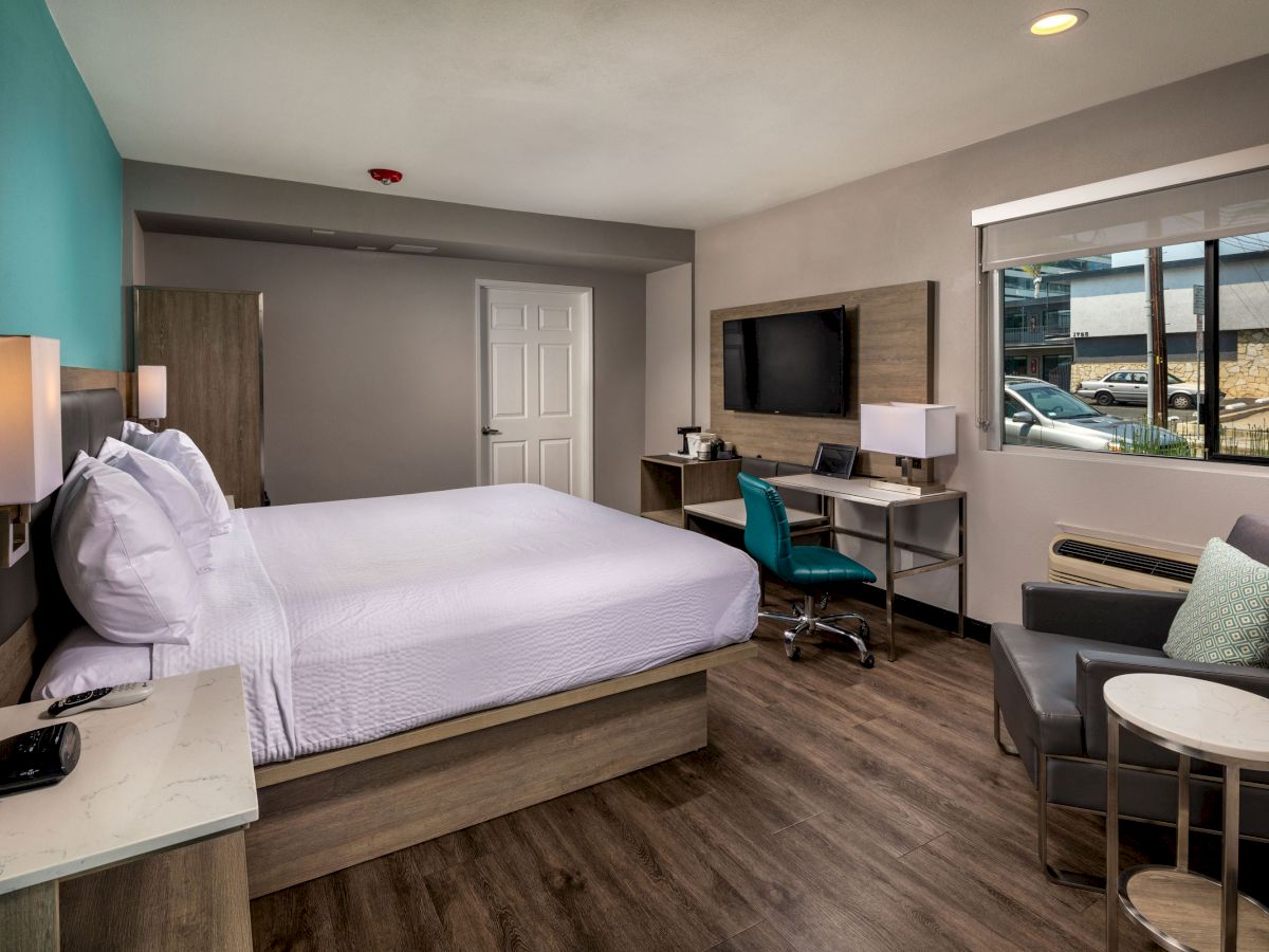 This image shows a modern hotel room with a bed, desk, chair, television, and seating area by the window, with a clean and organized appearance.