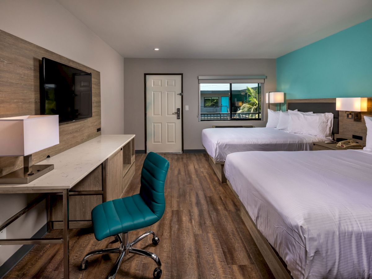 A modern hotel room with two double beds, a desk with a lamp, a TV, a chair, and a window; the decor is minimalist with wooden flooring.