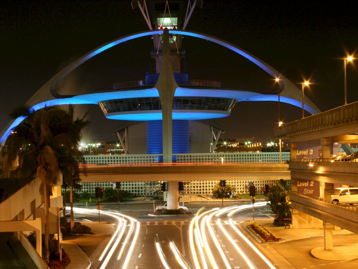 Nighttime image of a futuristic building with blue lighting features an arched structure and surrounding traffic with light trails.