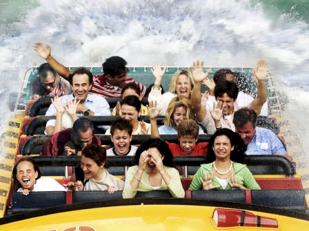 A group of people are riding a water-themed amusement park ride at "Jurassic Park," with water splashing around them and expressions of excitement.