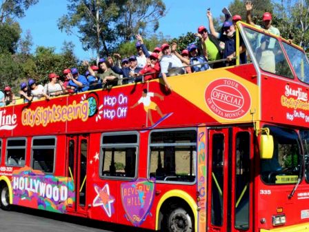 A double-decker bus labeled "StarLine City Sightseeing" with passengers on top, passing by lush greenery on a sunny day.