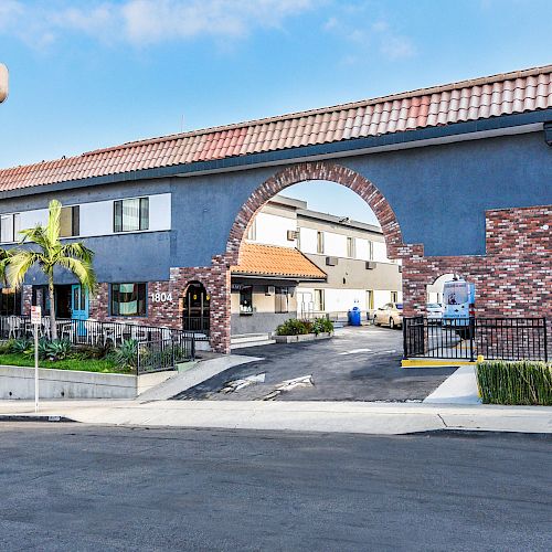 This image shows the exterior of a Travelodge hotel with an archway entrance, blue sign, and a mix of brick and stucco façade.