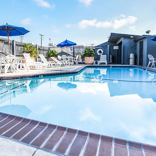 A clear swimming pool with lounge chairs and blue umbrellas around it, set in a peaceful outdoor environment that looks inviting for relaxation.